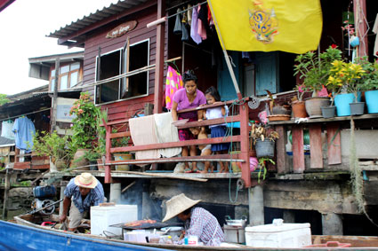 Una vendedora de un puesto ambulante prepara unas brochetas a la brasa, mientras una familia de la ribera espera su comanda, (Bangkok)